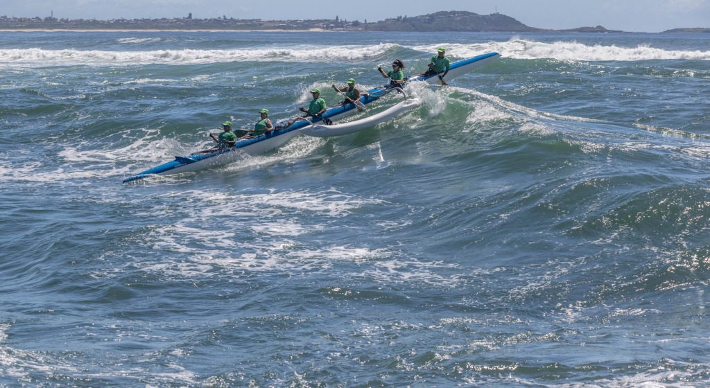 A crew of OC6 paddlers surfing a swell